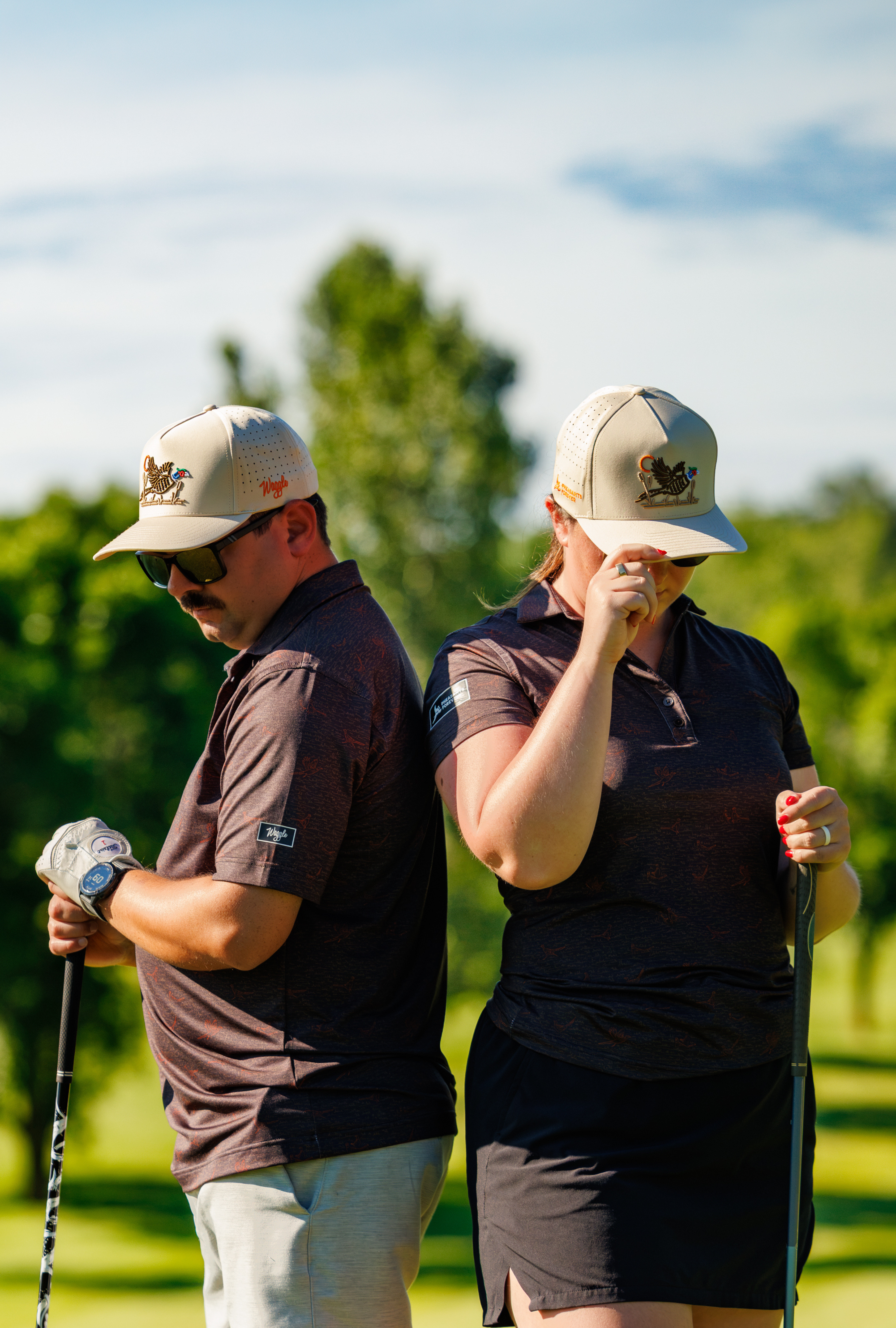 Two golfers standing on a green course, wearing pheasant and quail themed golf apparel, holding golf clubs.