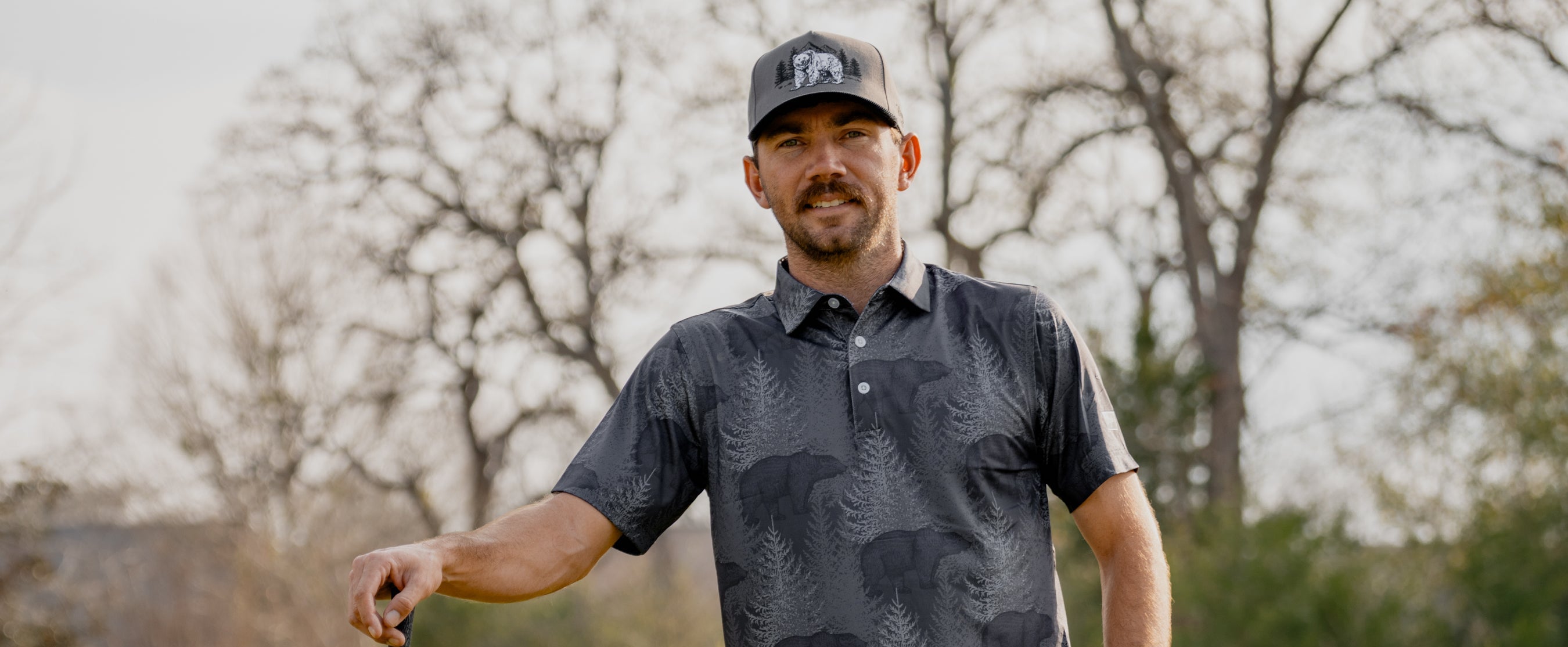 Chandler Phillips holding a golf club outdoors with trees in the background wearing Waggle