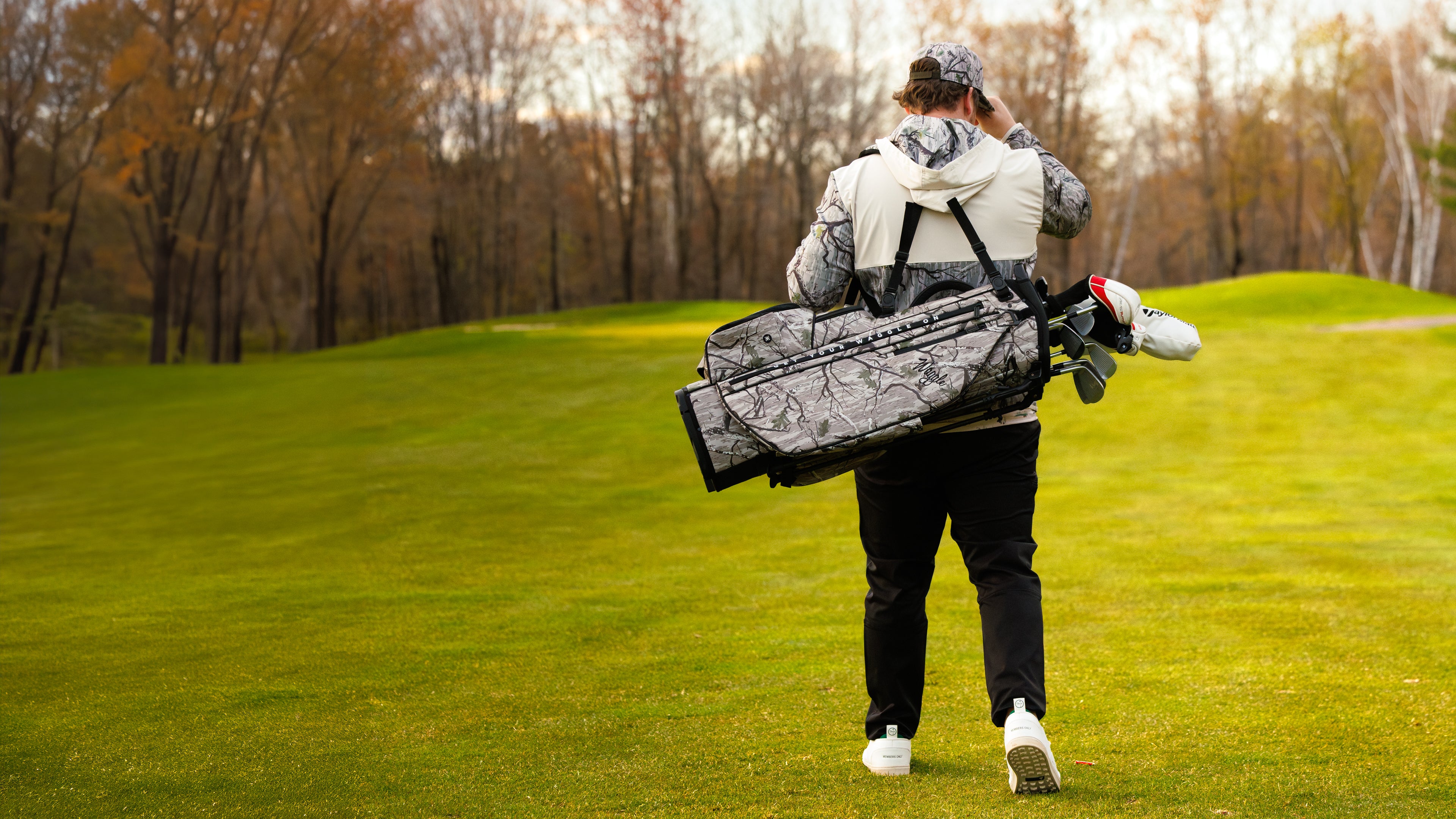 Man walking away wearing camo hoodie and golf bag.