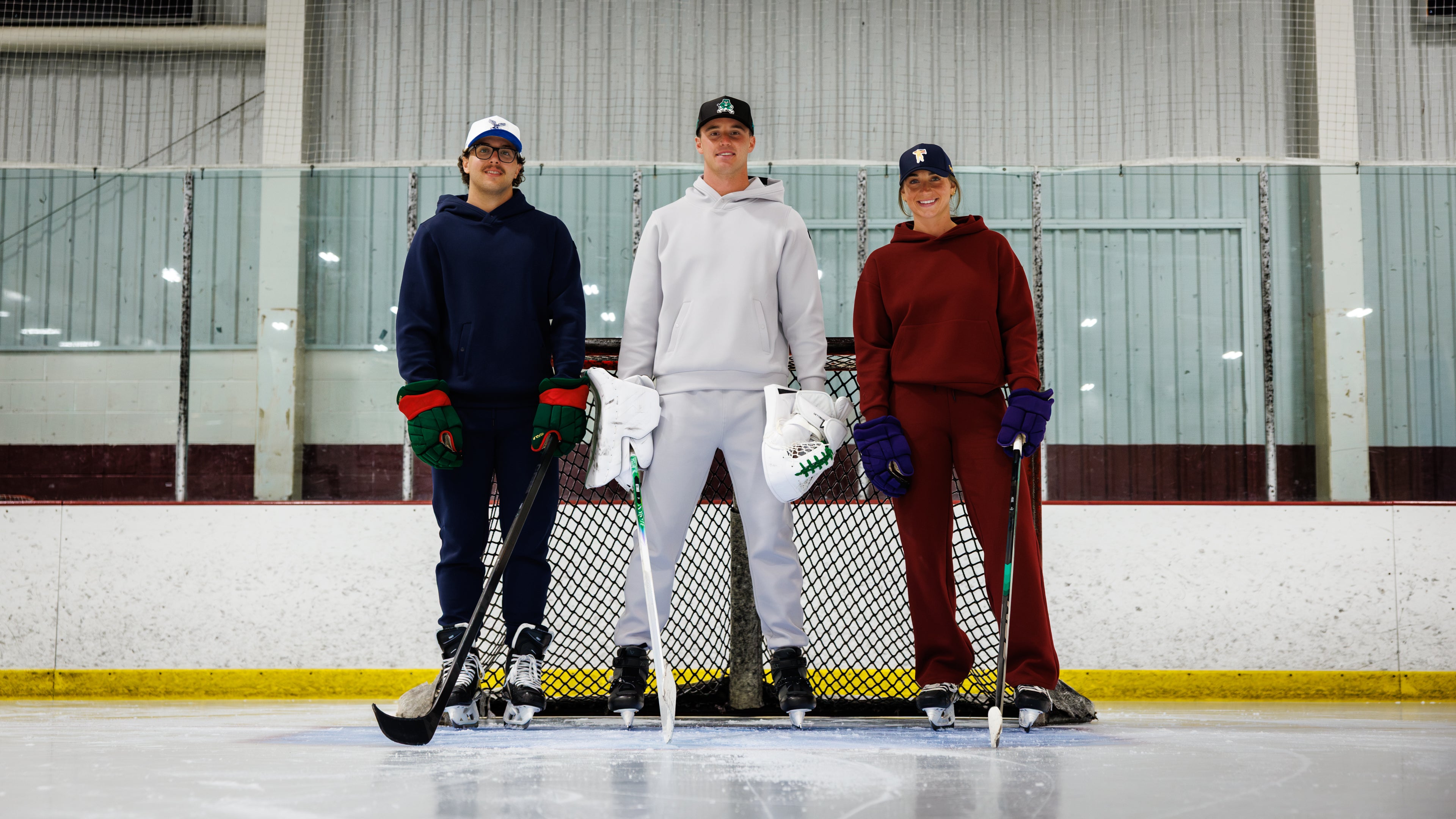 Brock Faber, Jake Oettinger, and Taylor Fox standing together in front of an indoor ice rink goal, wearing sweat sets in navy, light gray, and burgundy.