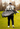 A man on a golf course seen from behind, carrying a camouflage golf bag over his shoulder on a golf course.
