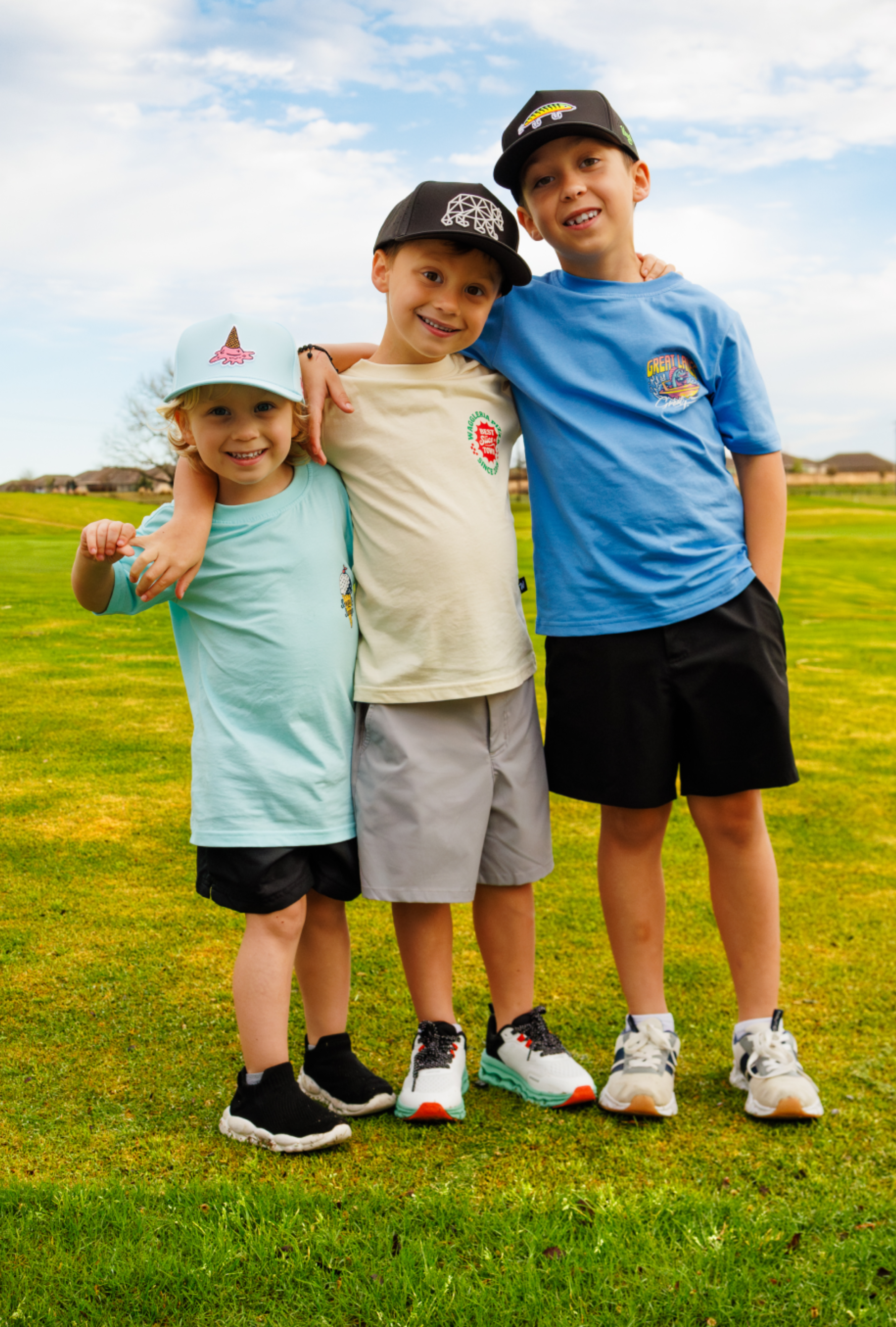 Three children standing together outside, wearing t-shirts and snapbacks.