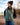 Model wearing the Balsam Crosscut Vest outside on a rock beach with trees and blue sky in the background