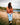 Female Model wearing the Frontier Wildknit Sweater sitting on a rocky shoreline with a lake and trees in the background.