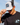 Model wearing the Galactic Greens Trucker Hat doing a hat tilt with blue sky as the background