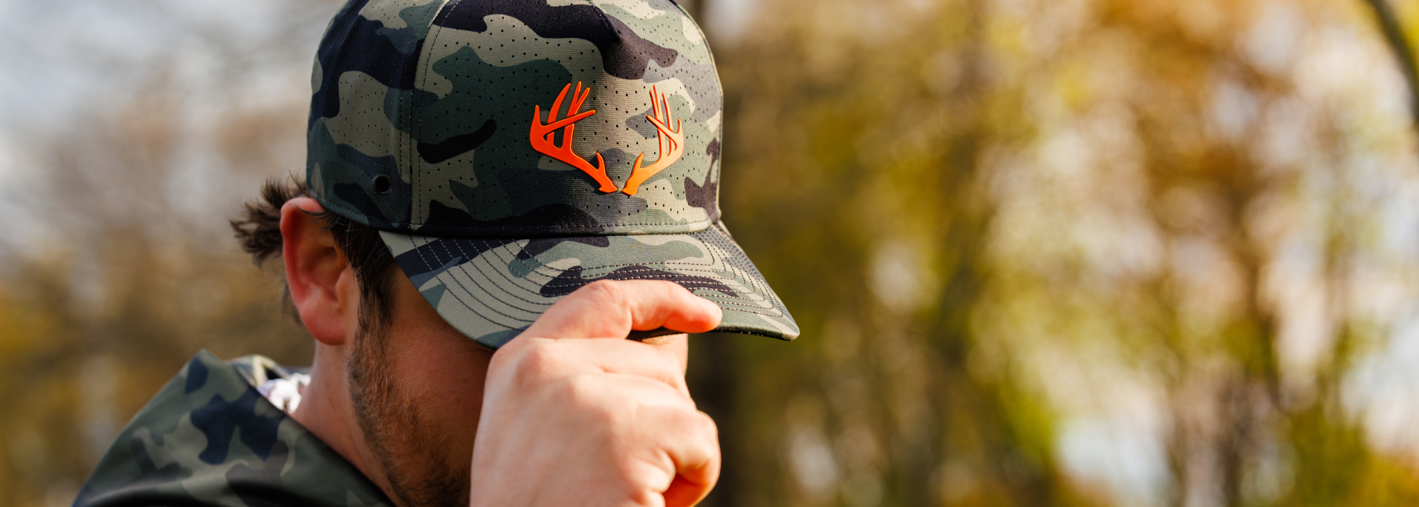 Man holding camo hat, outdoors.