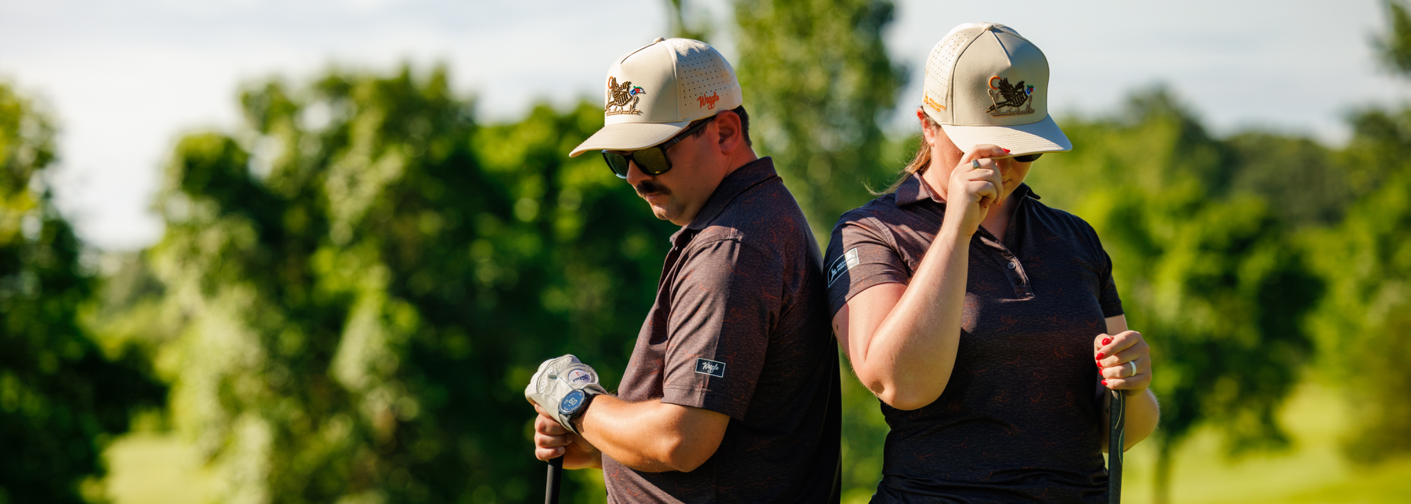 Two golfers standing on a green course, wearing pheasant and quail themed golf apparel, holding golf clubs.