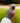 Model wearing the Wildflower Way Sleeveless Polo on the golf course preparing for a shot with a bunker and greenery in the background.